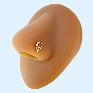 Detail of a gold nose stud featuring a red heart zircon and S-shaped metal curve on model