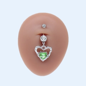 Détail d'un piercing de nombril argenté avec pendentif double cœur et cristal vert