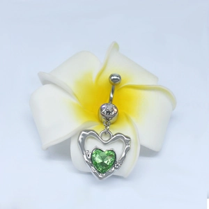 Détail d'un piercing nombril en argent avec zircon coeur vert et pendentif croix