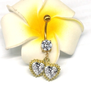 Detail eines goldenen Herz-Bauchnabelpiercings mit klaren Steinen und Perlenrand