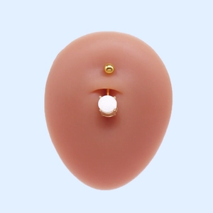 Détail d'un piercing de nombril doré avec pierre blanche sur un modèle de peau