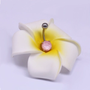Détail d'un piercing de nombril pailleté rose placé dans une fleur de frangipanier