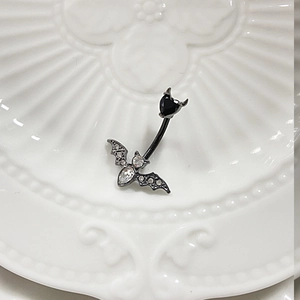 Detail of bat navel ring with black heart gem and white crystals on a white plate