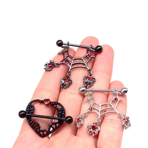 Detailansicht von gotischen Spinnennetz- und Herz-Schädel-Brustpiercings mit roten Steinen