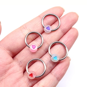 Detailed shot of four colorful heart nipple rings on hands with glowing beads