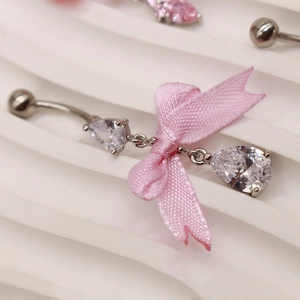 Nahaufnahme von silbernem Bauchnabelpiercing mit rosa Schleife und Zirkonia in Tropfenform
