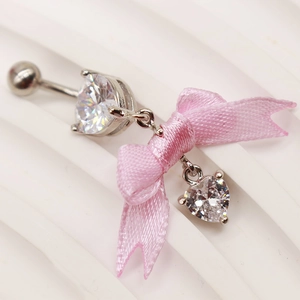 Detailansicht eines silbernen Bauchnabelpiercings mit rosa Satinschleife und Herz-Zirkonia