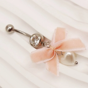 Detailaufnahme des rosa Samtbogens und Herz-Perlenanhängers am Bauchpiercing