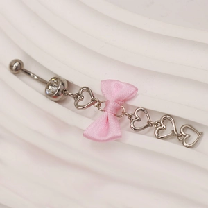 Makroaufnahme Bauchnabelpiercing mit rosa Satinschleife und funkelnden Herz-Zirkonia