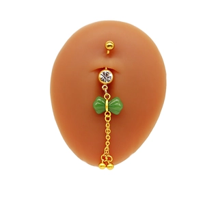 Detailed shot of belly button ring featuring green bow pendant and dangling golden chains