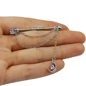 Dettaglio di un piercing industriale argento con catene e ciondolo luna e stella
