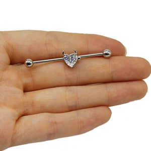Dettaglio del piercing industrial con pietra a cuore e corna da diavolo in acciaio