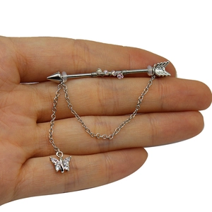 Macro dettaglio del piercing industriale freccia argento con perle rosa e pendente a farfalla