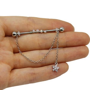 Dettaglio piercing industriale con ciondolo a stella, catena pendente e perle trasparenti
