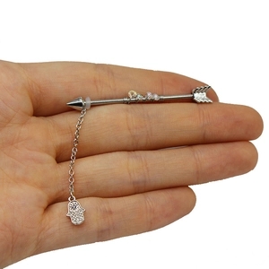 Dettaglio piercing industriale con freccia, pendente mano di fatima e perle colorate