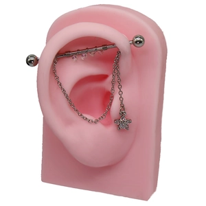 Dettaglio piercing industriale con catena d'argento e ciondolo a fiore in zircone su orecchio