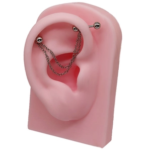 Dettaglio piercing industriale con doppia catena su un modello di orecchio in silicone