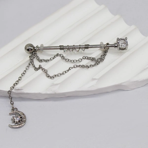 Dettaglio piercing industriale con ciondolo luna e stella e catenine in argento lucido