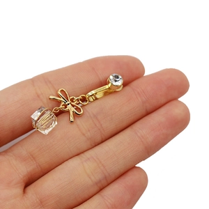 Dettaglio di una clip per ombelico dorata con fiocco, perline di cristallo e strass