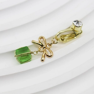 Dettaglio di un orecchino a clip dorato con perla a cubo verde e design a fiocco