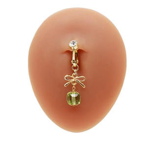 Dettaglio di un piercing all'ombelico dorato con fiocco e perla verde su un modello