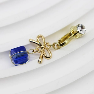 Dettaglio dell'orecchino a clip a fiocco dorato con perla blu e strass bianco