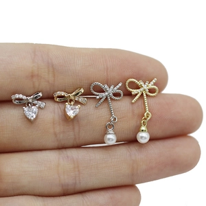 Detail of bow-knot labret studs with heart-shaped zircon and pearl charms in hand