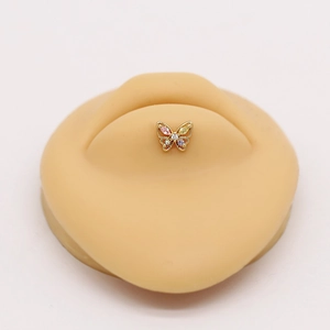 Golden butterfly labret piercing with colorful cubic zirconia on a silicone model