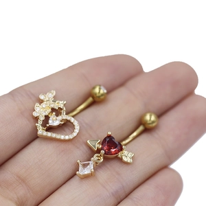 Piercings de ombligo dorados con corazón de circonia y flecha de Cupido en fondo blanco