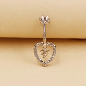 Primer plano de un piercing de ombligo plateado con colgante de corazón y circonita