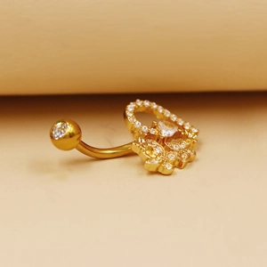 Vista macro de piercing para ombligo dorado con colgante de corazón y circón blanco