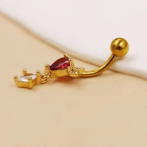 Detalle de un piercing de ombligo dorado con corazón rojo y circón transparente