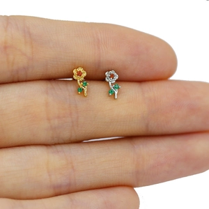 Macro detail of tiny floral labret studs with red gemstones and green crystals