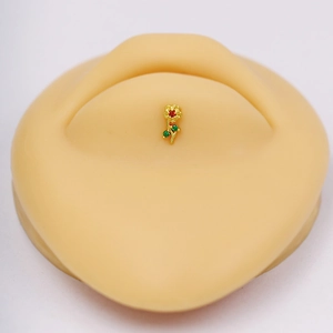 Macro view of gold flower piercing stud with red stone and green leaf accents