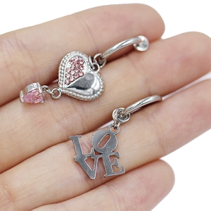 Makroansicht von Herz und LOVE-Buchstaben Bauchnabelpiercing auf einer Fingerspitze