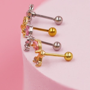 Detalle macro de piercings dorados y plateados con cristales de circón rosa en forma de flor