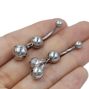 Detalle de un par de piercings para el ombligo en acero inoxidable con colgantes de campana