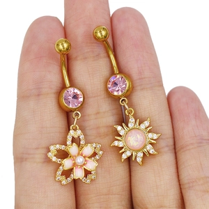 Vue détaillée de piercings de nombril dorés avec fleur de cerisier en perle et soleil en opale