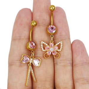 Détail de piercings de nombril dorés avec papillon et pierres roses tenus dans la main