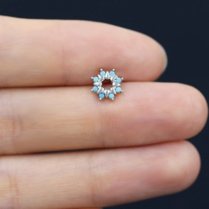 Macro shot of a tiny silver floral earring with blue stones held on a fingertip
