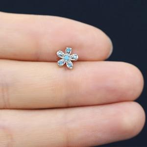 Macro shot of a tiny silver flower earring with five blue zircons held by fingers