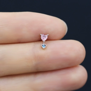 Macro view of pink and blue heart-shaped zirconia studs held on fingertips for size