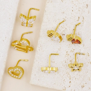Dettaglio di 7 piercing al naso a L dorati con design a farfalla, cuore e corona reali