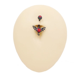 Detalle de piercing de ombligo gótico con circón de corazón rojo y alas de murciélago
