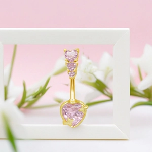 Close-up of golden navel ring featuring pink heart-shaped zircons and tiny gold stars