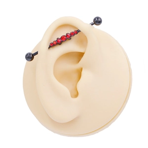 Detail of black industrial barbell with red rhinestones on a silicone ear model