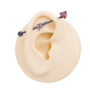 Detail of black industrial barbell earring with red heart stone and silver pistol charm