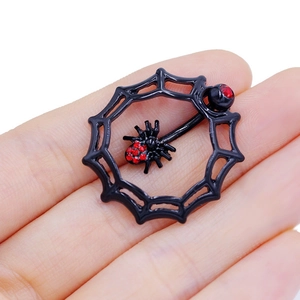 Detailed view of black spider web nipple ring with red cubic zirconia held by hand