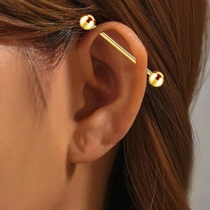Close-up of a gold titanium industrial barbell piercing on an ear cartilage