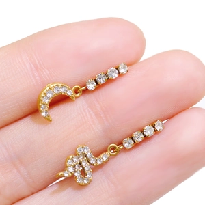 Close-up of golden moon and snake earrings with sparkling crystals held between fingers